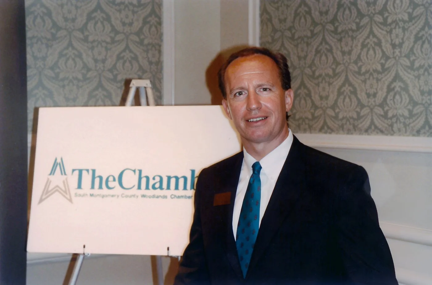 Congressman Brady in front of a sign bearing the logo of The South Montgomery County Woodlands Chamber of Commerce.